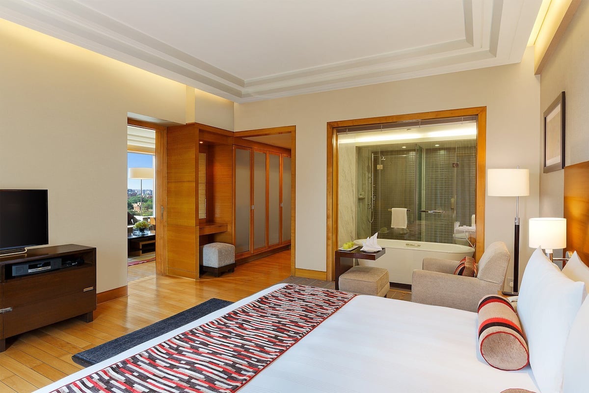 A hotel room with a bed, a TV, a desk, a chair, and a bathroom with a mirror and shower.