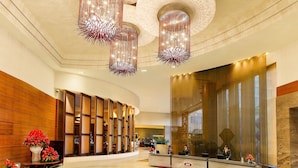 Un vestíbulo amplio con una mesa de recepción, candelabros modernos y un gran muro de cristal.