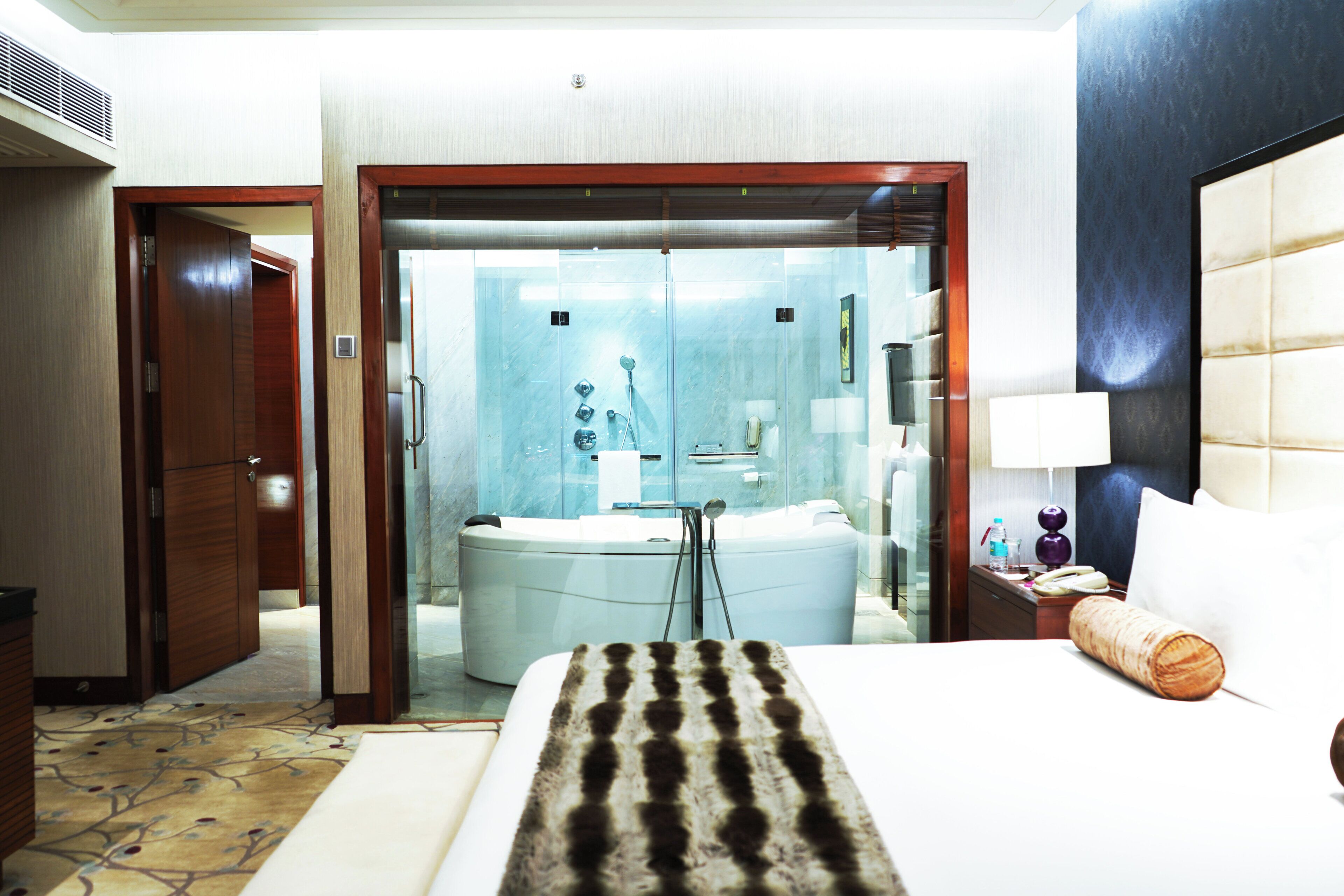 A hotel room with a bed, a bathroom with a bathtub, and a large mirror.