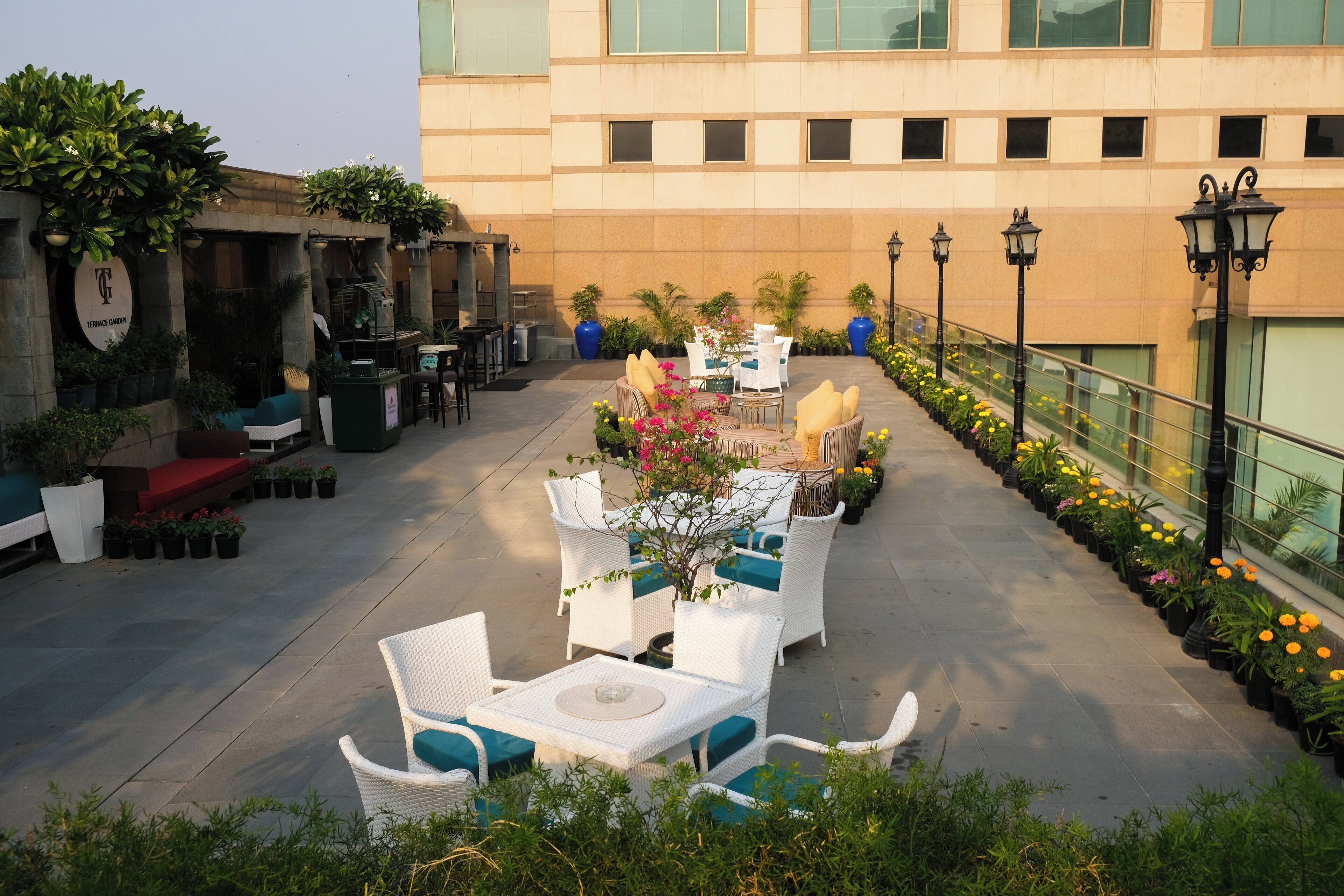 An outdoor patio area with white wicker furniture, potted plants, and a railing with street lamps.