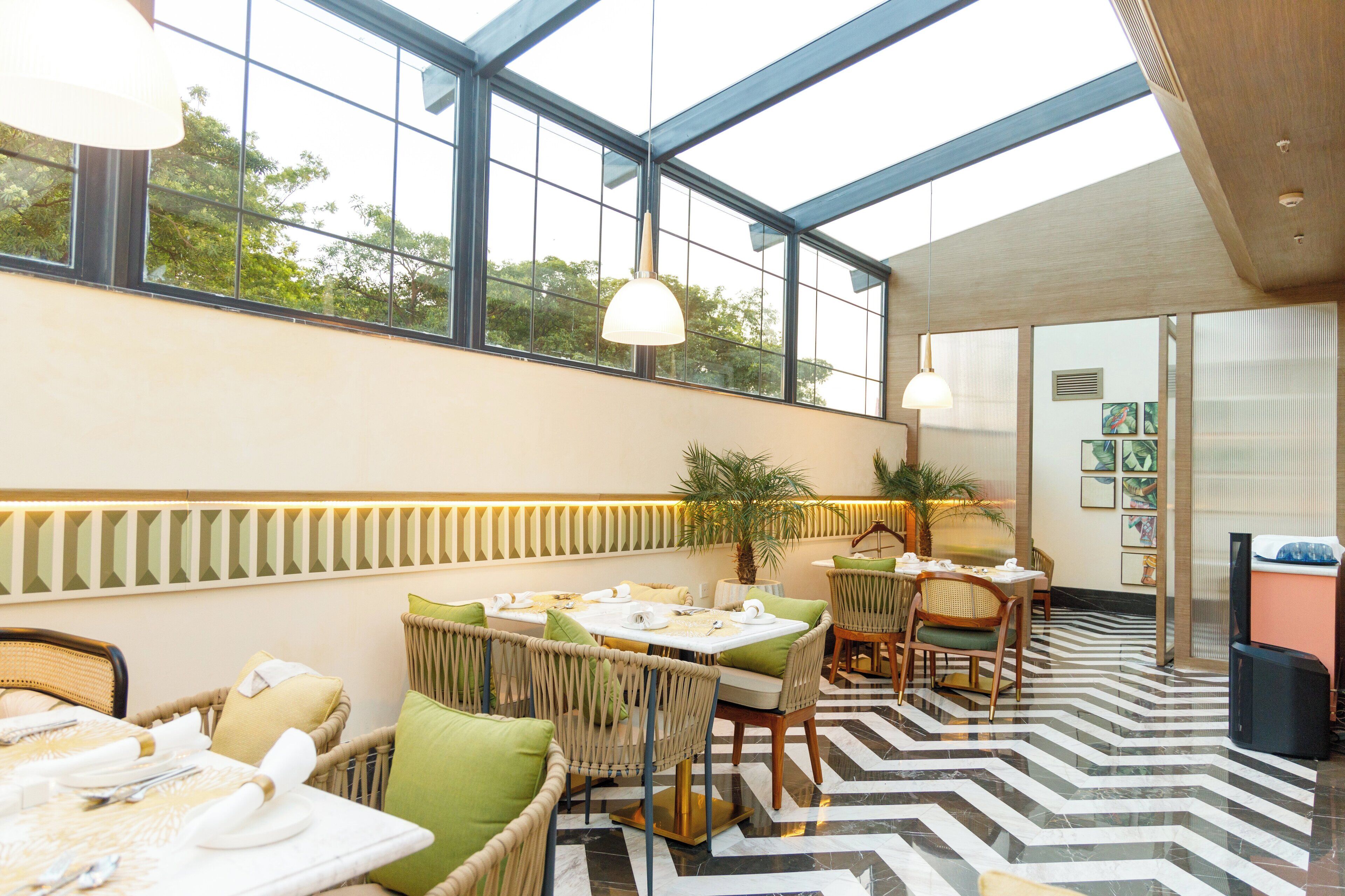 A dining area with wicker furniture, a black and white patterned floor, and large windows with a view of greenery.