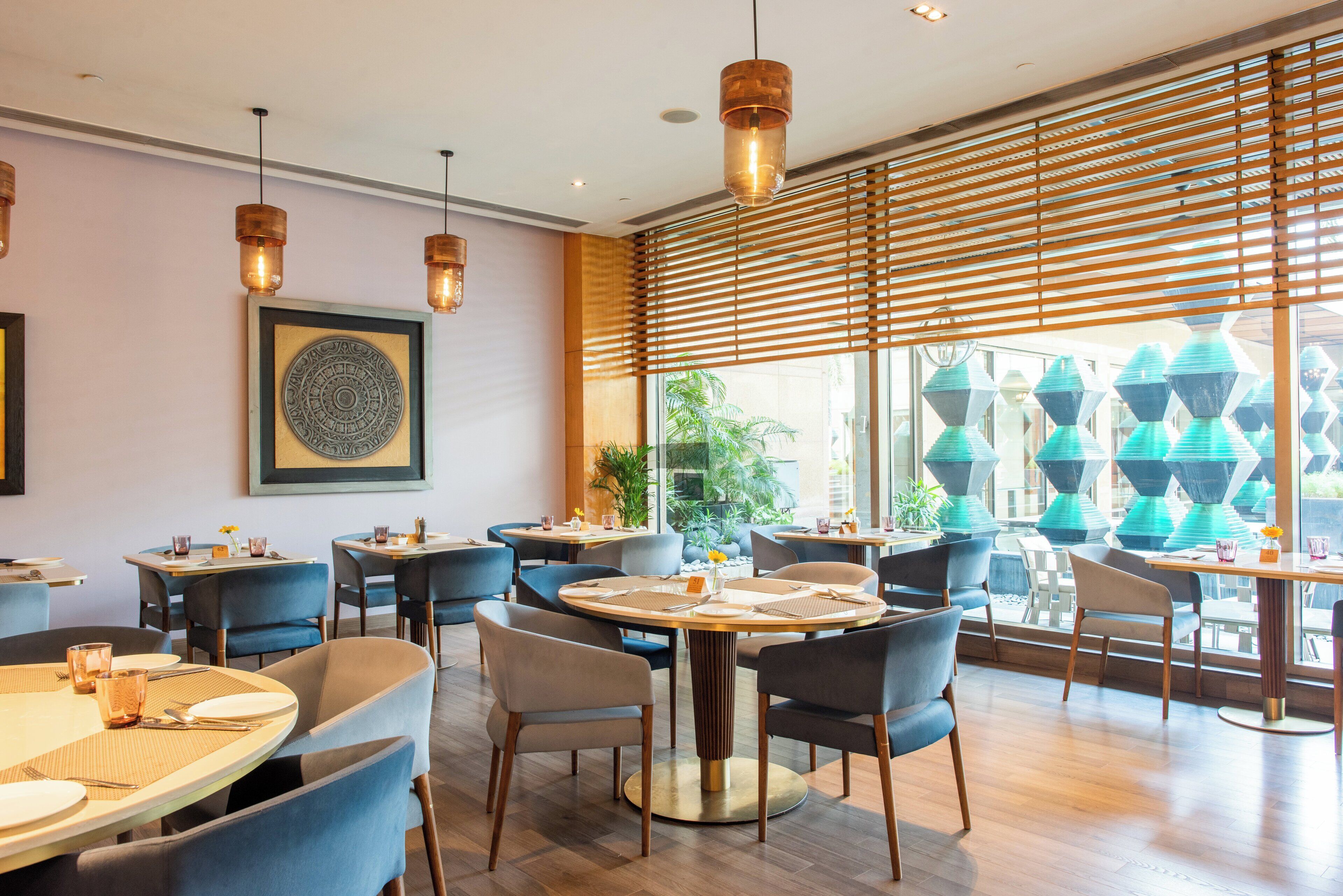 Un interior de restaurante moderno con mesas redondas, sillas azules e iluminación colgante.