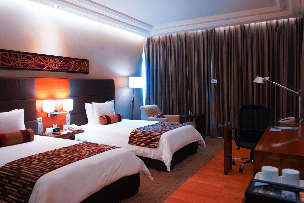 A hotel room with two beds, a desk, a chair, a lamp, and a curtain.