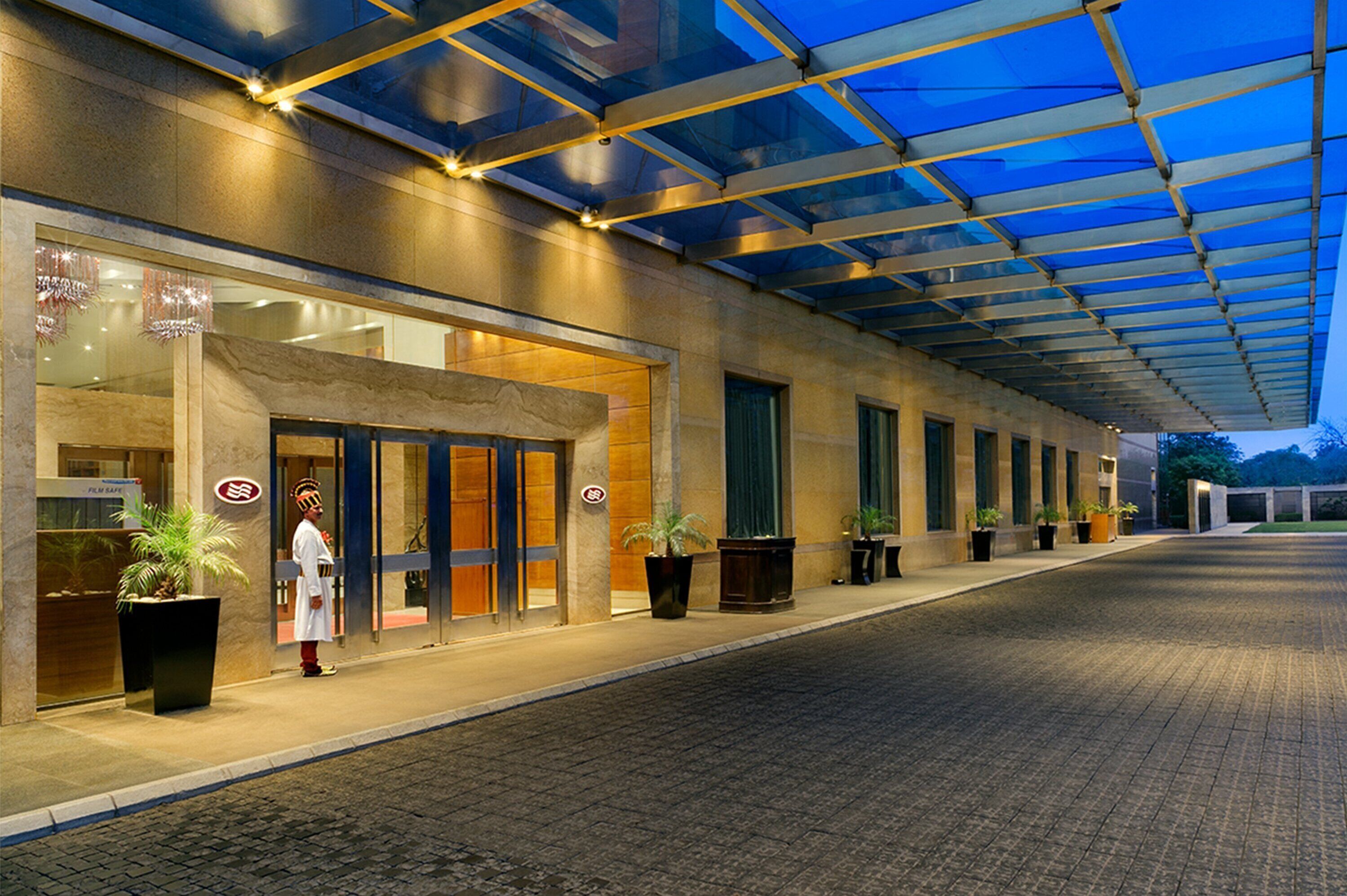 L’entrée d’un hôtel, avec un passage couvert, des plantes en pot et un employé en uniforme.