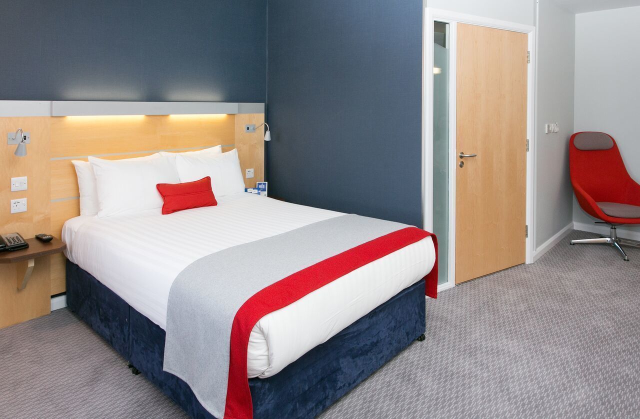 Une chambre d’hôtel avec un lit, une table de chevet, une chaise rouge et une porte.
