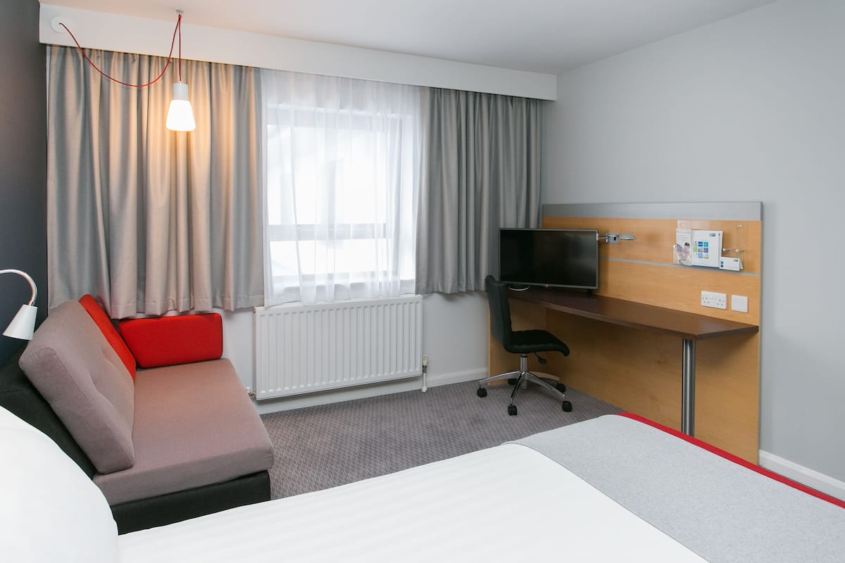 A hotel room with a bed, a desk, a chair, a TV, and a window with curtains.