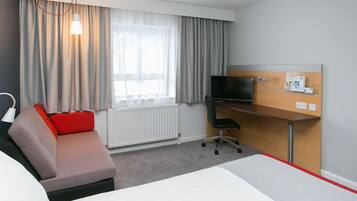 Habitación de hotel con cama, escritorio, silla, televisor y ventana con cortinas.