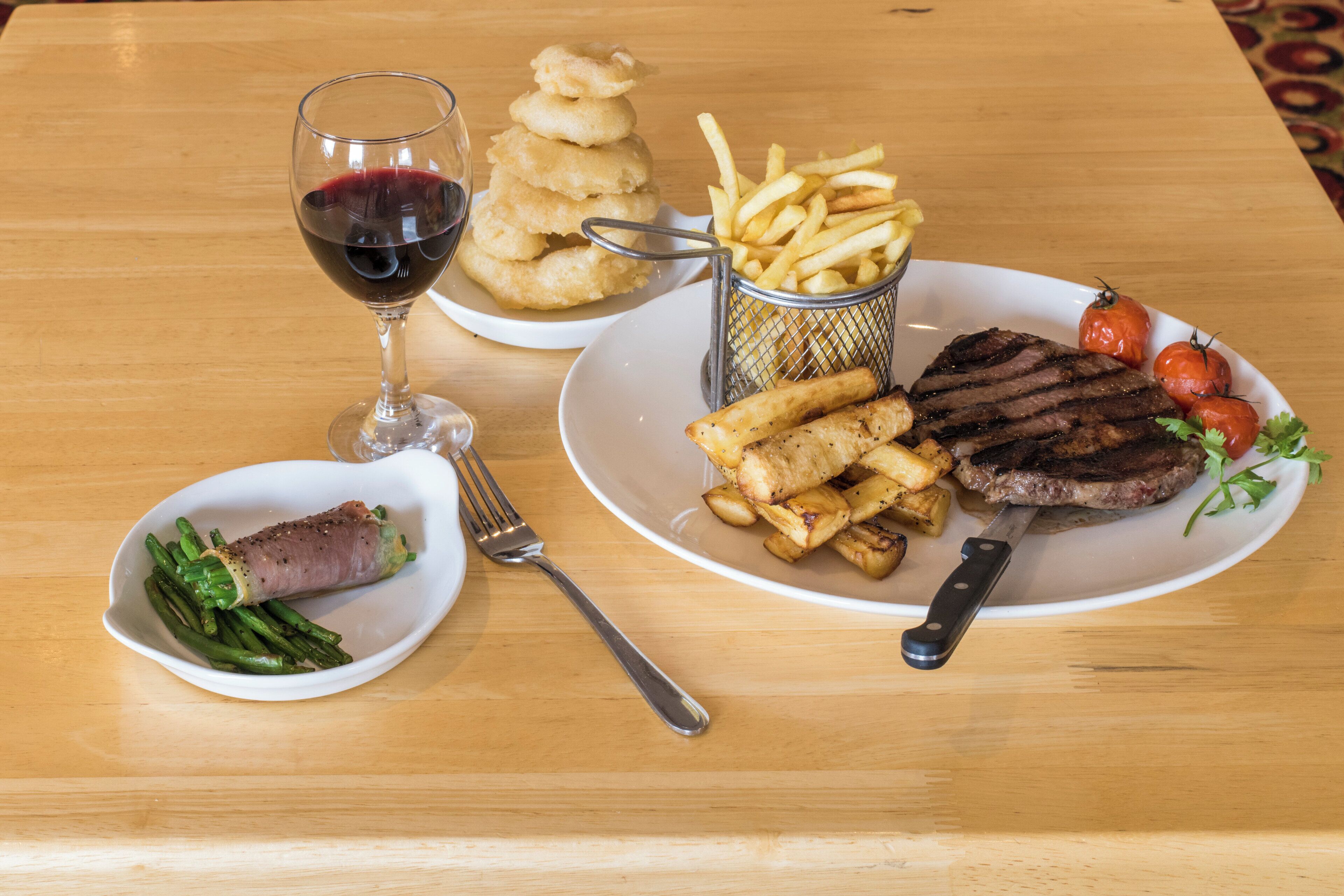 A dining table with a plate of food including steak, fries, and a glass of red wine.
