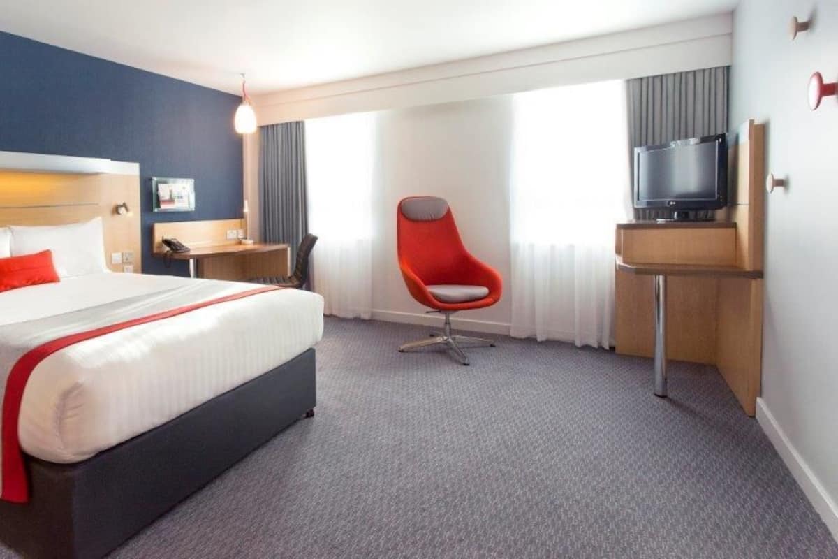 A hotel room with a bed, a desk, a chair, and a TV.