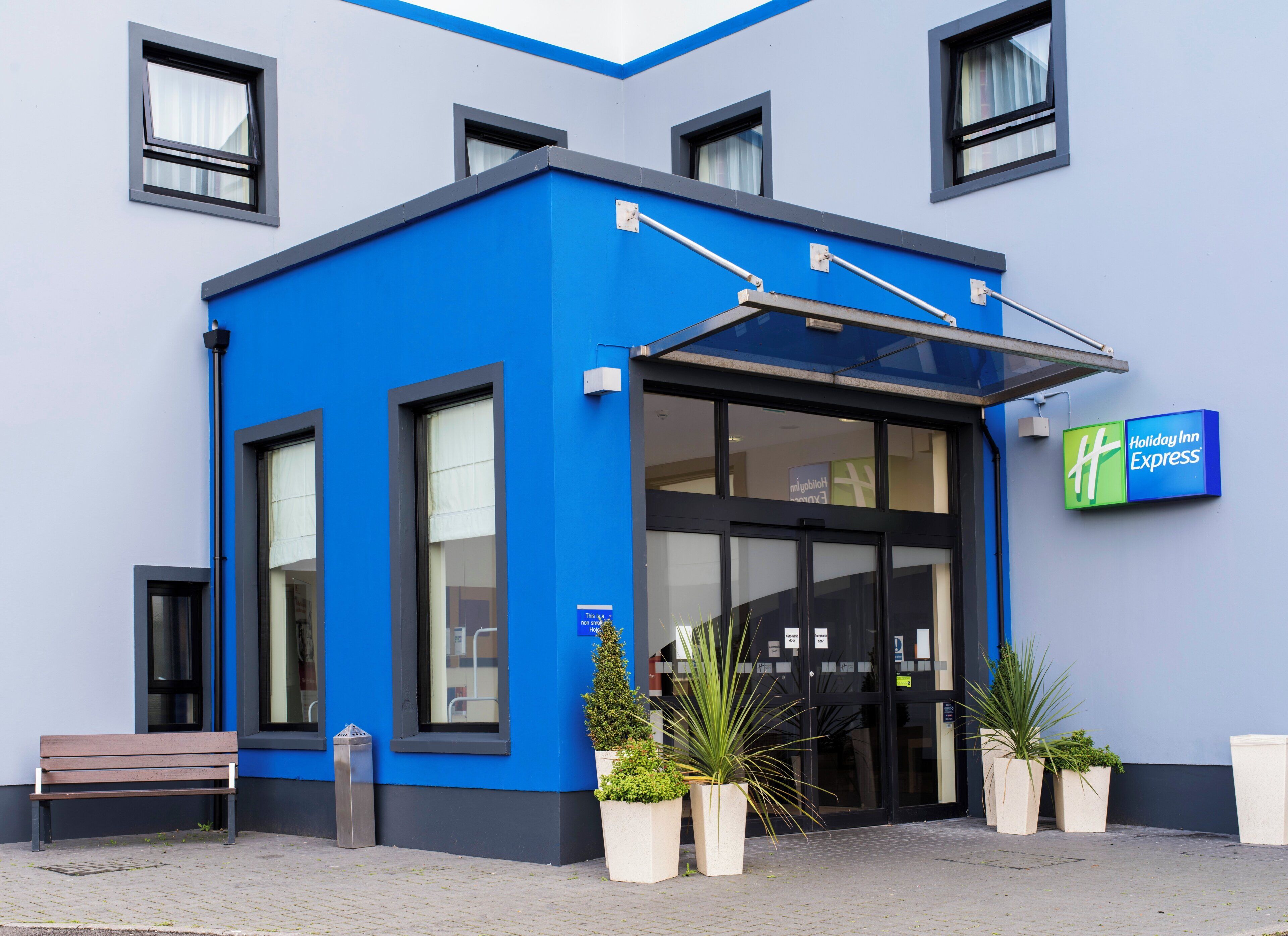 A Holiday Inn Express building with a blue exterior, large windows, and a bench outside.