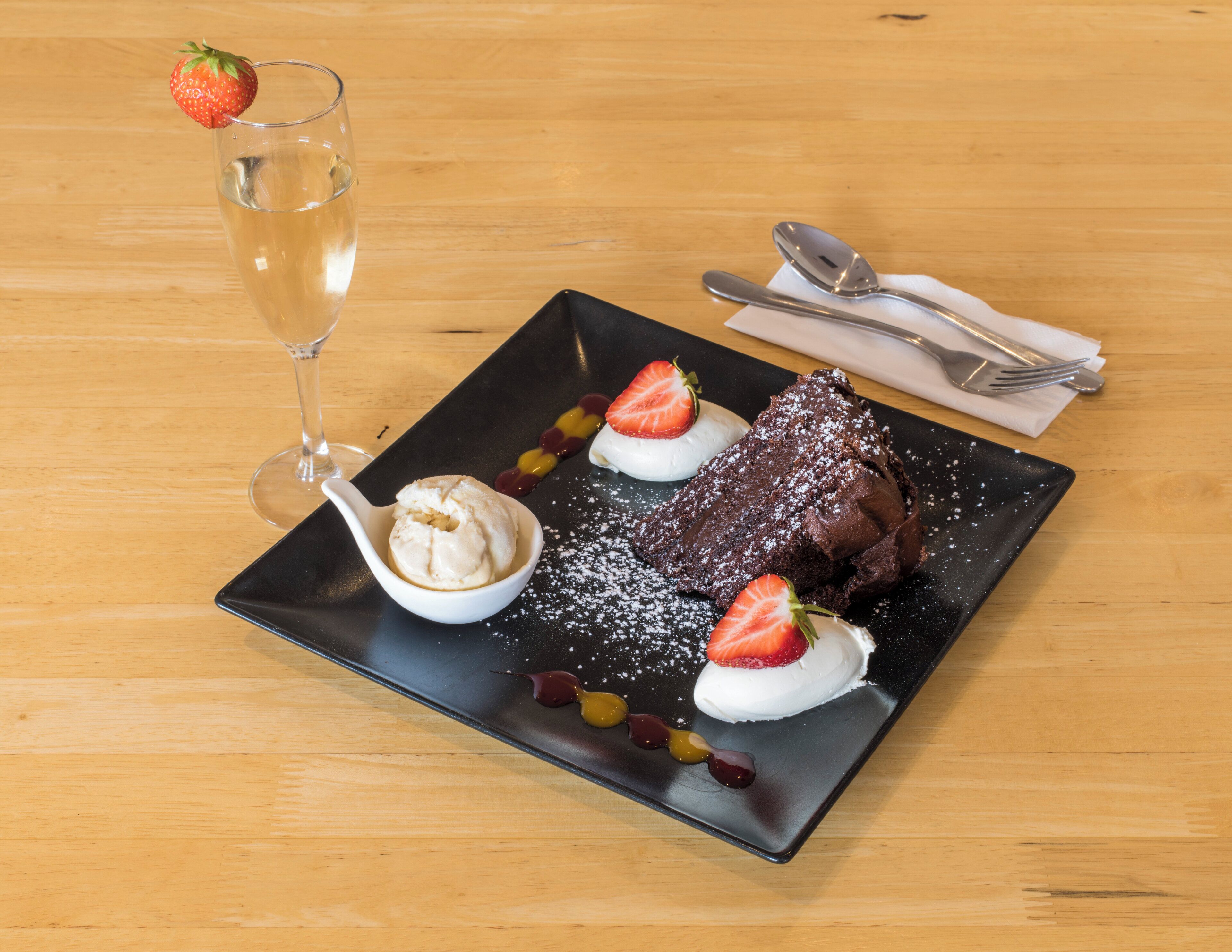 A dessert plate with a chocolate cake, whipped cream, strawberries, and a glass of a clear beverage.