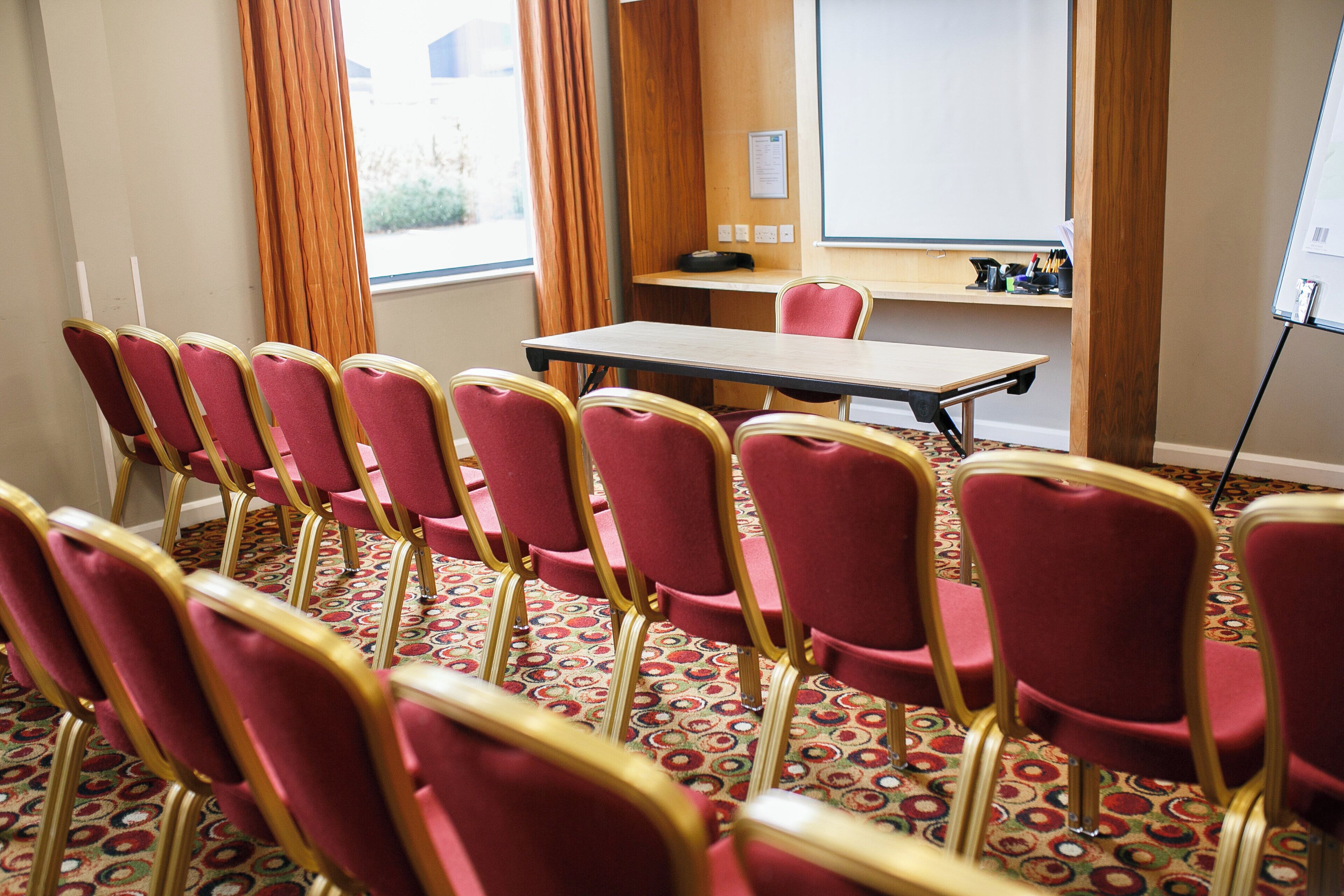 Une salle de conférence avec une longue table et des rangées de chaises rouges.