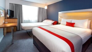 Habitación de hotel con dos camas, un escritorio con televisor y un ventanal con cortinas.