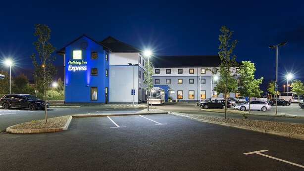 Edificio de Holiday Inn Express con fachada azul, estacionamiento y farolas.