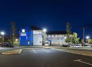 A Holiday Inn Express building with a blue exterior, parking lot, and street lamps.