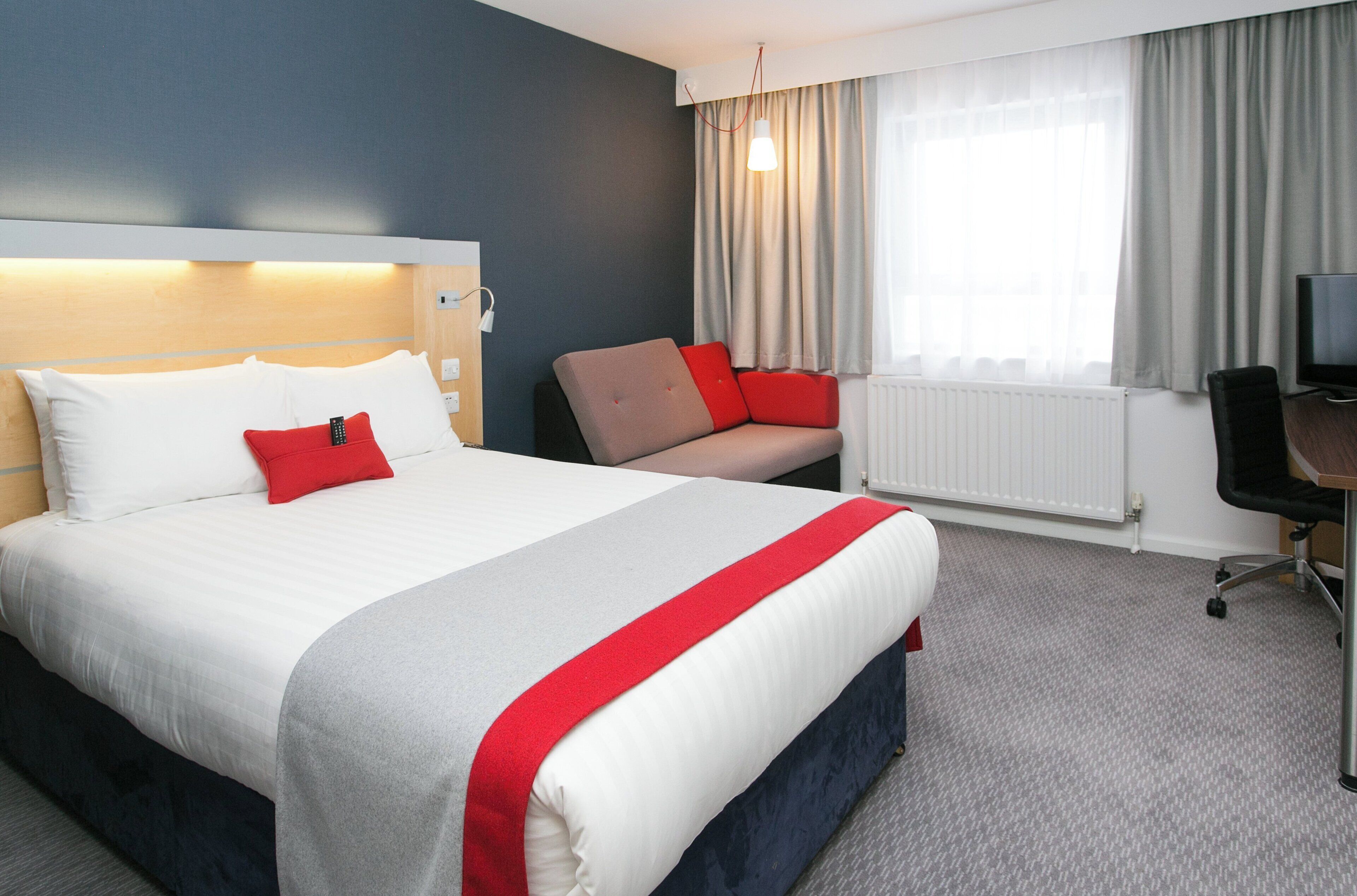 A hotel room with a large bed, a desk, a chair, and a television.