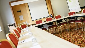Un salón de conferencias con una larga mesa, sillas rojas, una pantalla de proyector y piso alfombrado.