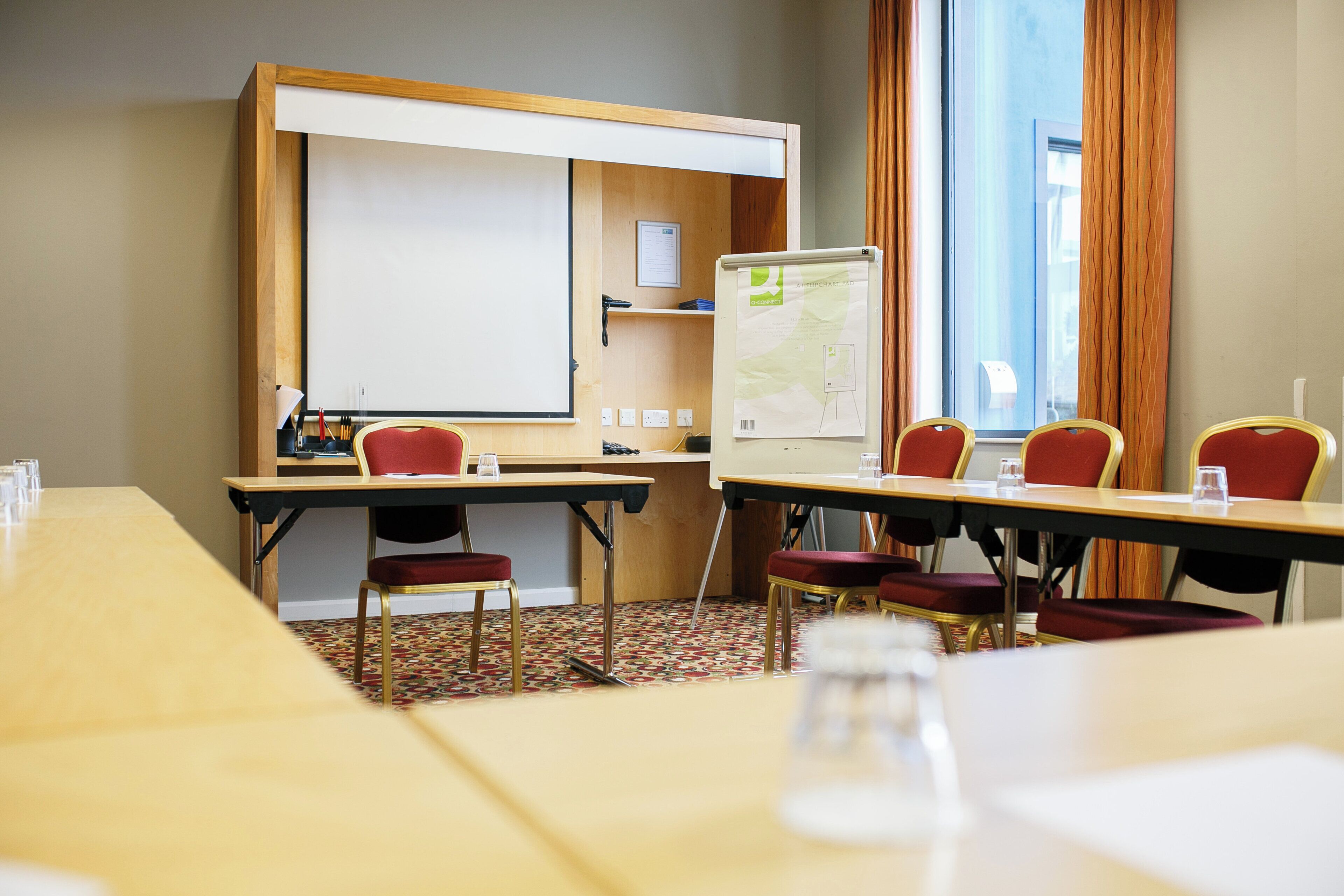 Una sala de conferencias con una pizarra, un rotafolio y una mesa con sillas.