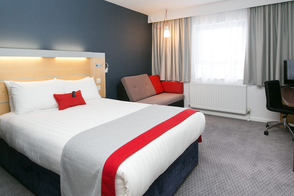 A hotel room with a large bed, a desk, a chair, a television, and a window with curtains.