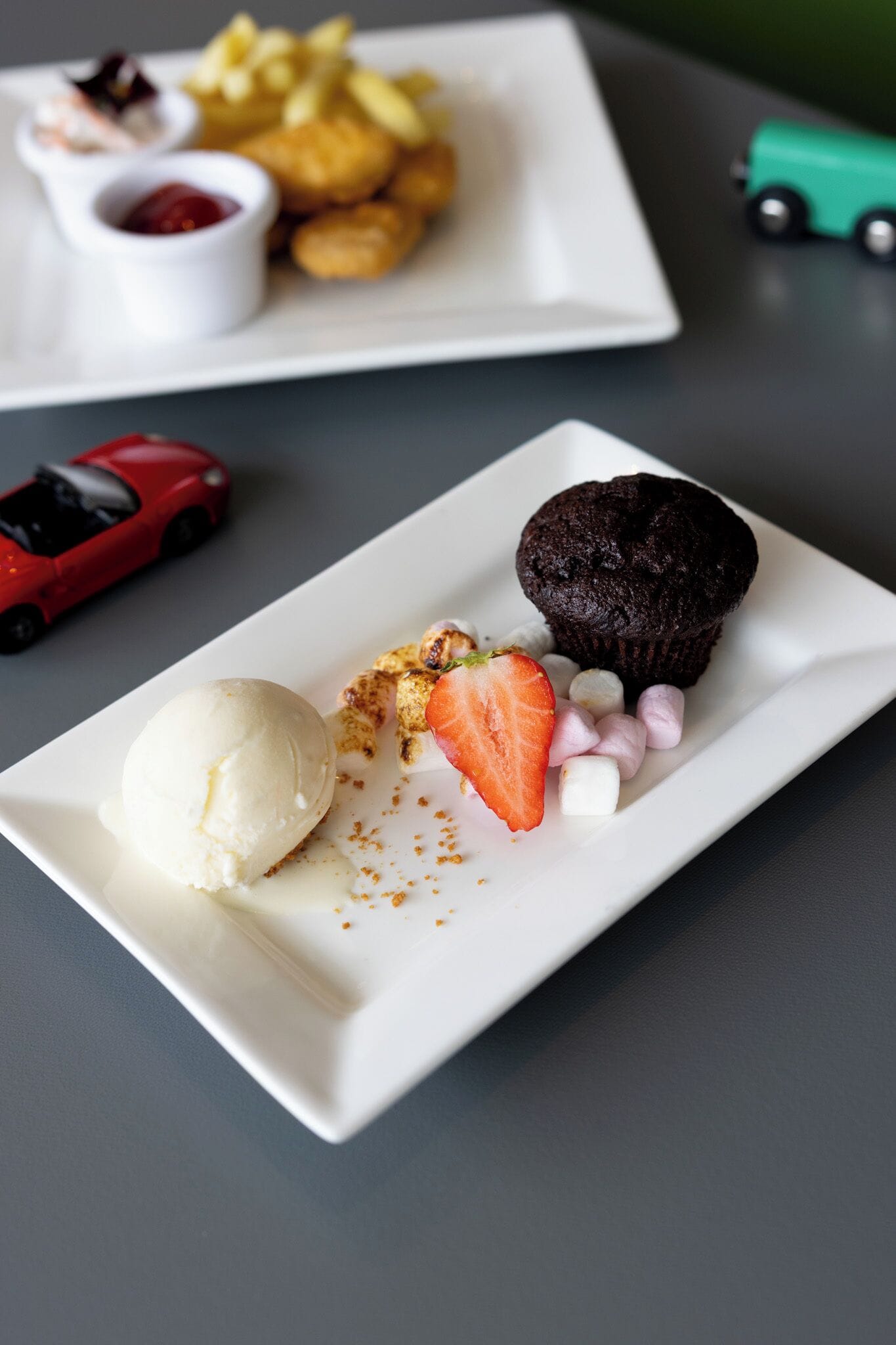 A dessert plate with a chocolate cupcake, a scoop of vanilla ice cream, a strawberry, and marshmallows.