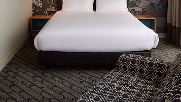 Habitación de hotel con una cama grande, cabecera con motivos de mariposas, mesita de noche y alfombra estampada.