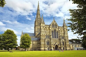 A large Gothic-style cathedral with multiple spires, surrounded by a grassy field and trees. - Holiday Inn Salisbury - Stonehenge by IHG (Salisbury)