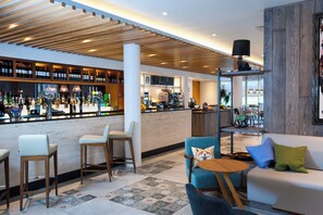 A modern bar area with a wooden ceiling, seating with cushions, and a variety of bottles on shelves. - Holiday Inn Salisbury - Stonehenge by IHG (Salisbury)