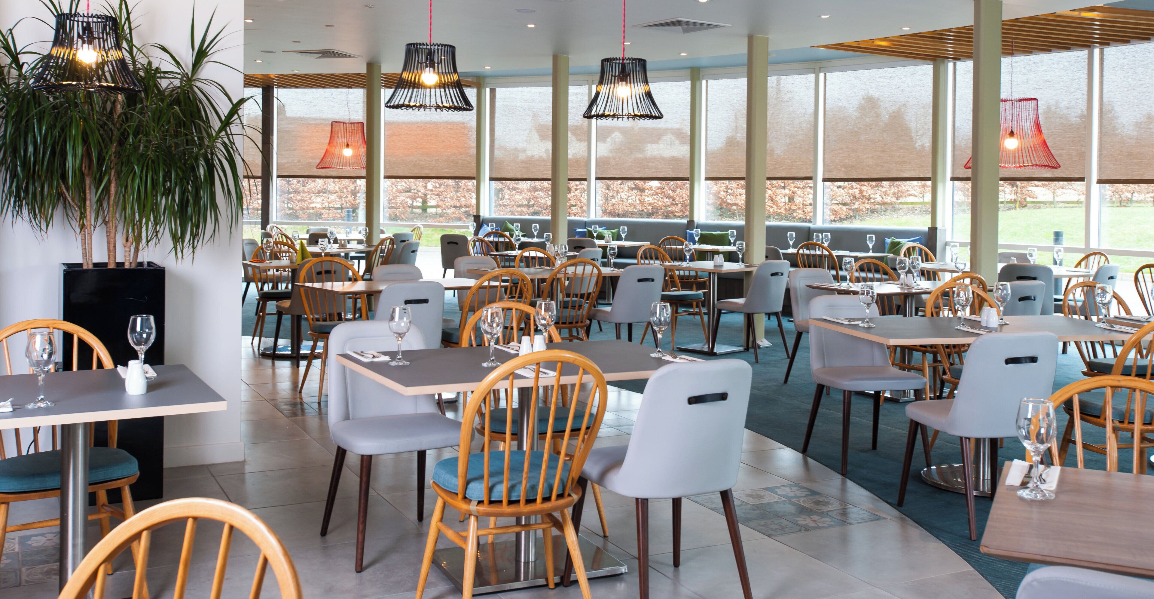 A restaurant with multiple tables and chairs, large windows, and hanging pendant lights.