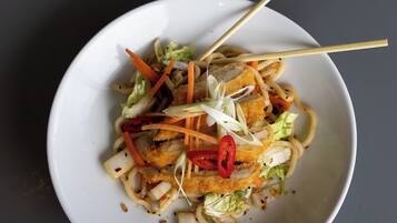 A bowl of noodles with vegetables and meat, served on a white plate with chopsticks.