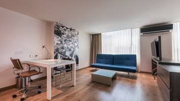 A modern living room with a sofa, a TV, a dining table with chairs, and a large abstract painting on the wall.
