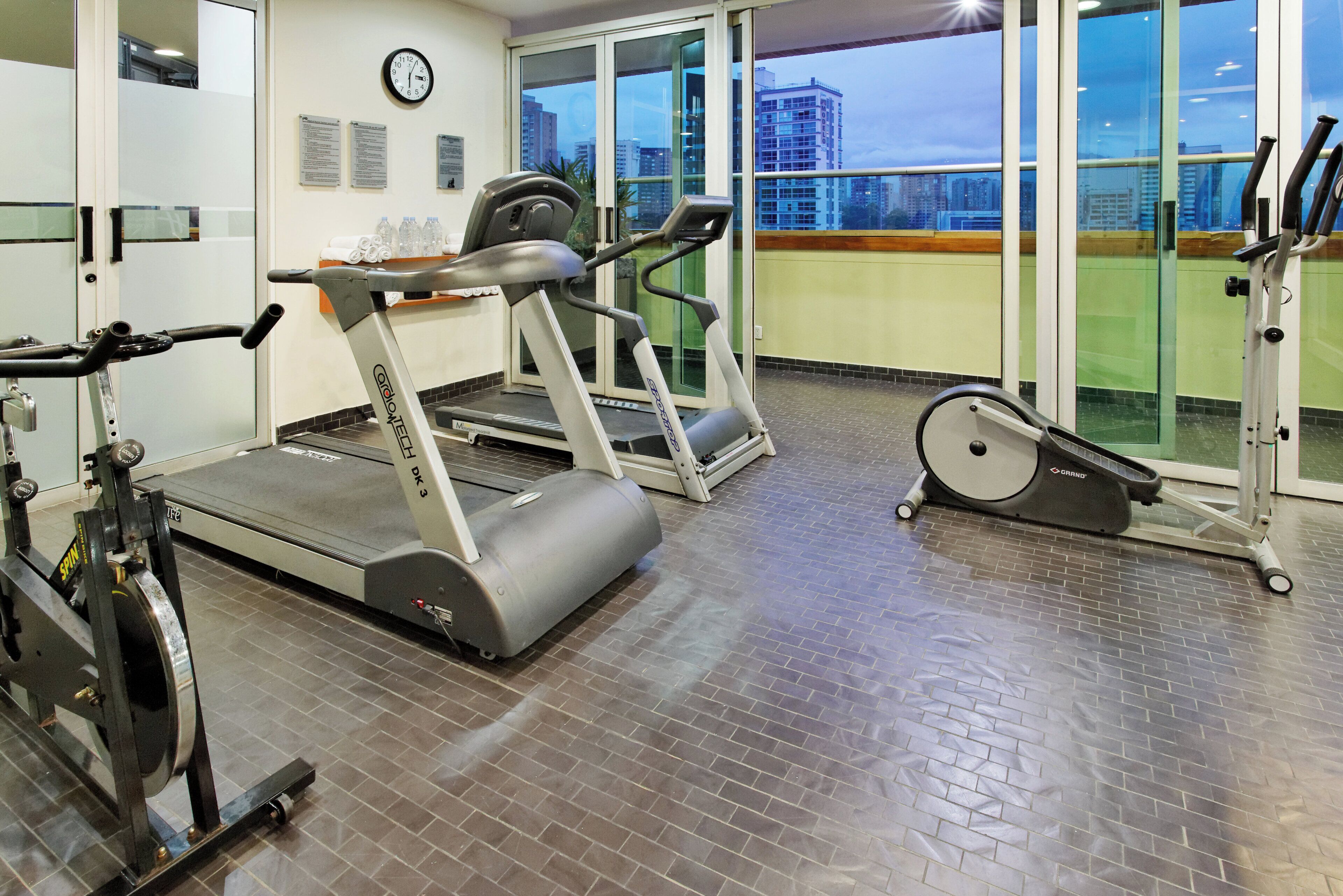 Un gimnasio con cintas de correr, bicicletas estáticas y un espejo grande.