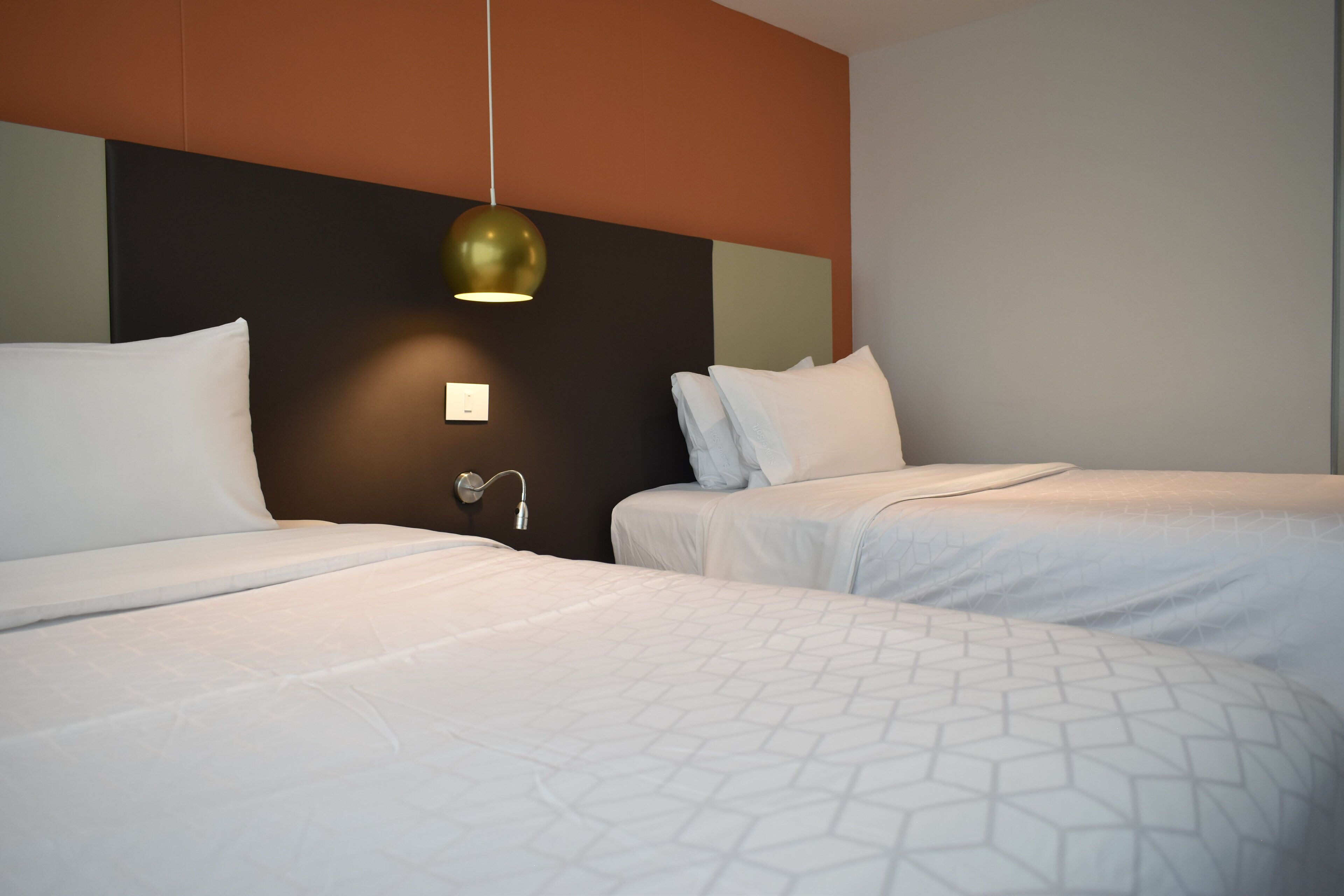 A hotel room with two beds, a modern pendant light, and a wall-mounted light switch.