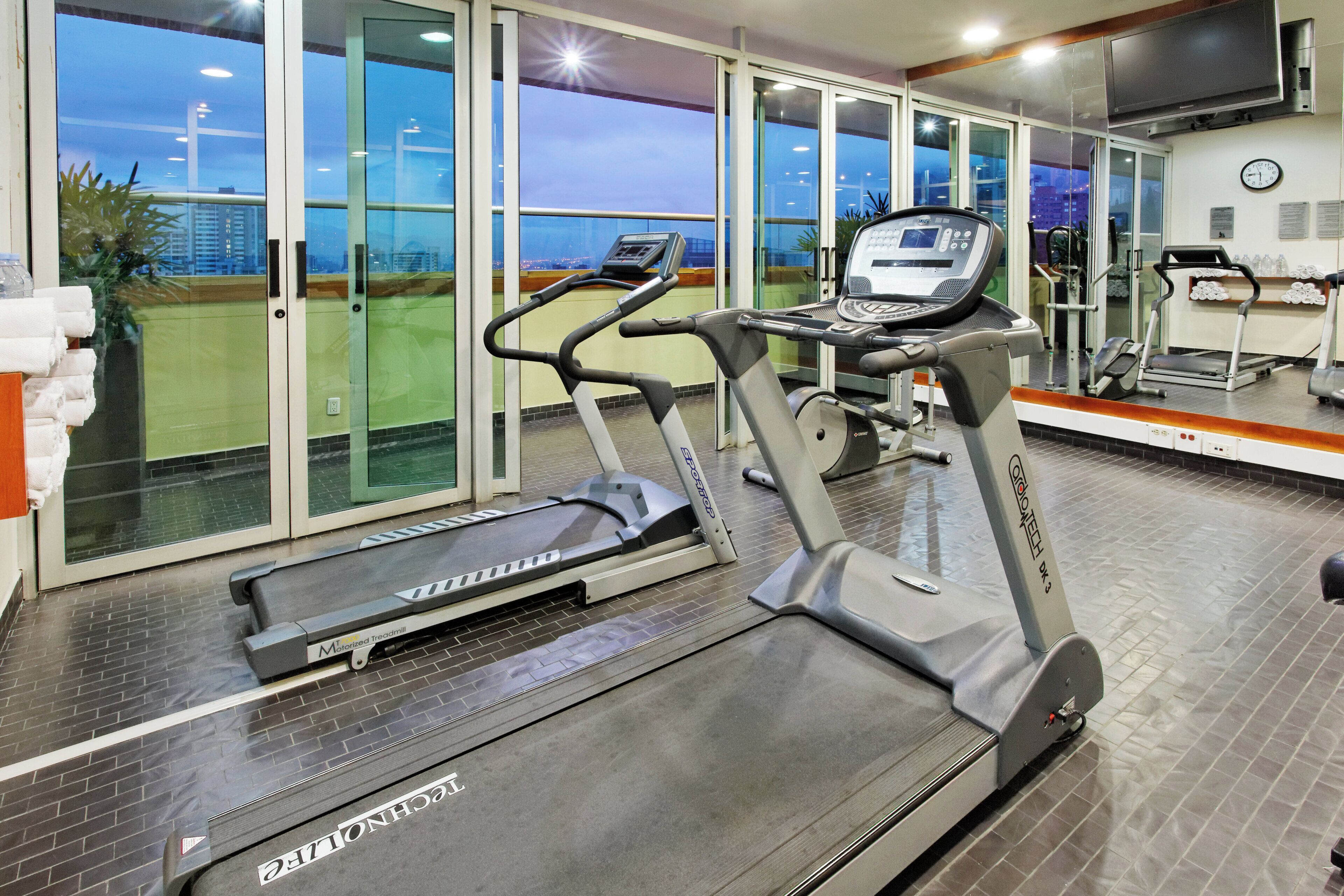 Un gimnasio con cintas de correr, bicicletas estáticas y un espejo grande.
