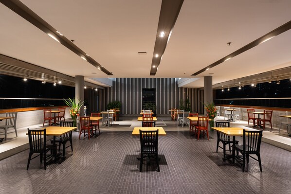 A spacious indoor dining area with multiple tables and chairs, a modern ceiling design, and large windows offering views of the night sky. - Holiday Inn Express Medellin by IHG (Medellín)