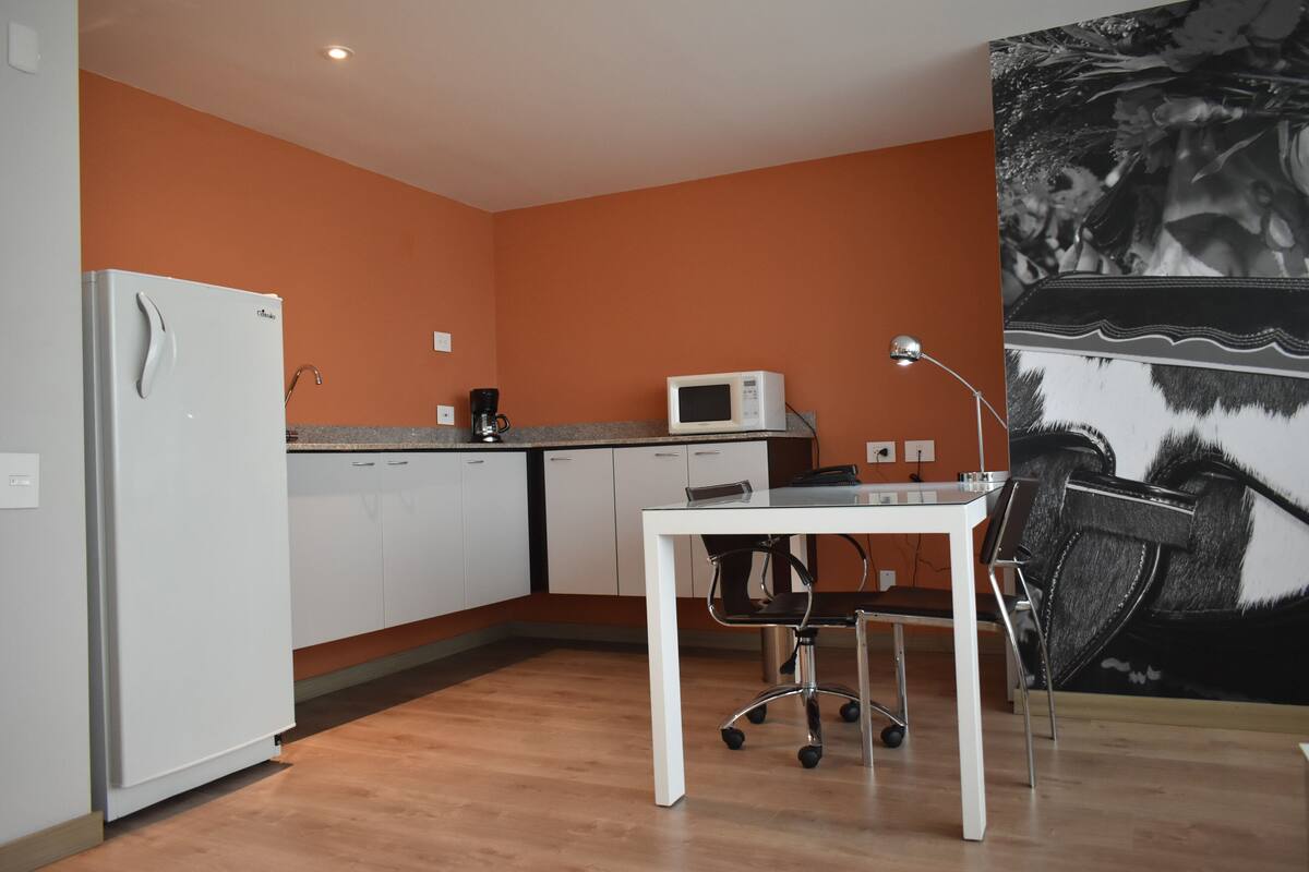 Una cocina compacta con armarios blancos, un refrigerador blanco, un microondas y una cafetera.