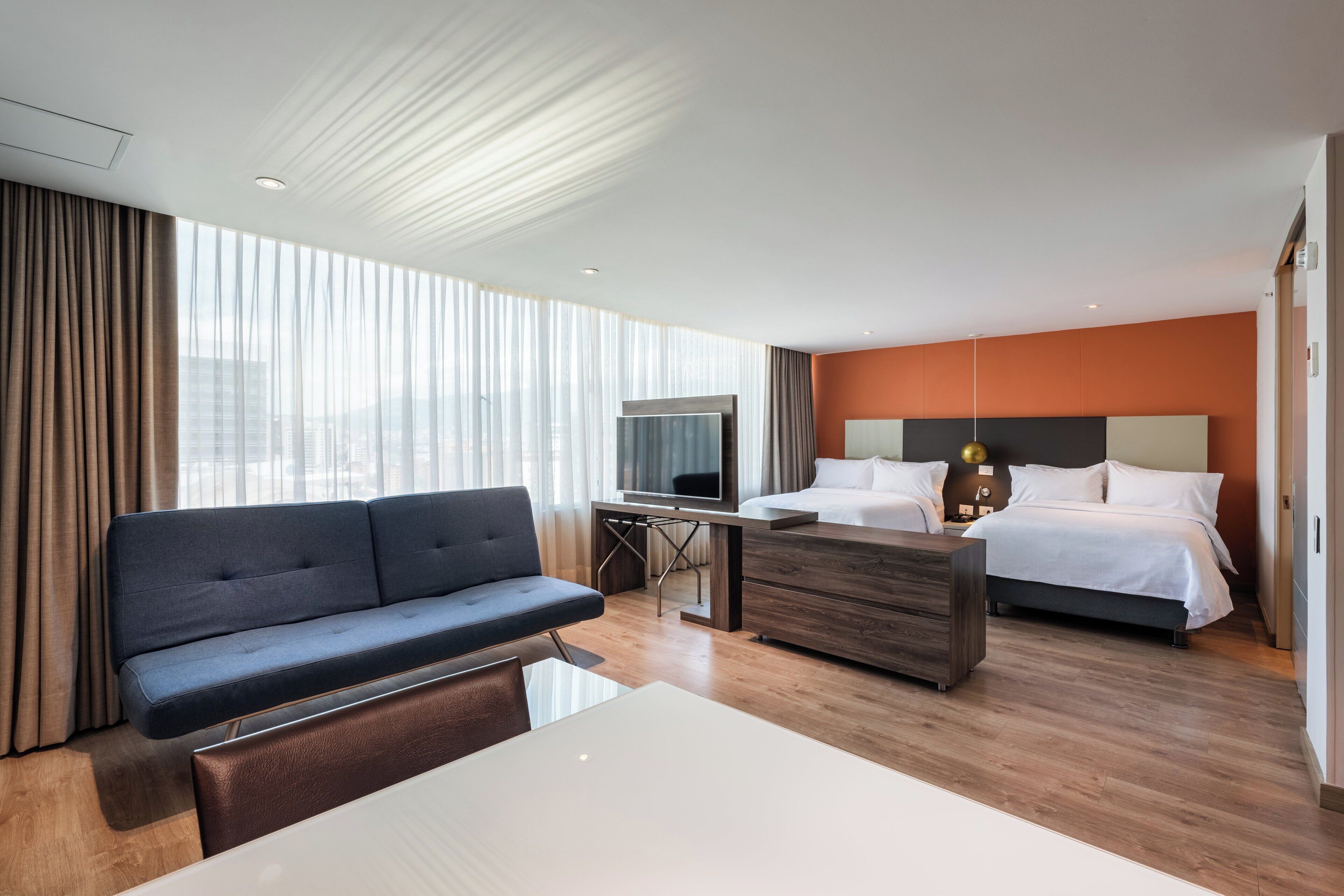 A modern hotel room with a sofa, a bed, a desk, and a television.