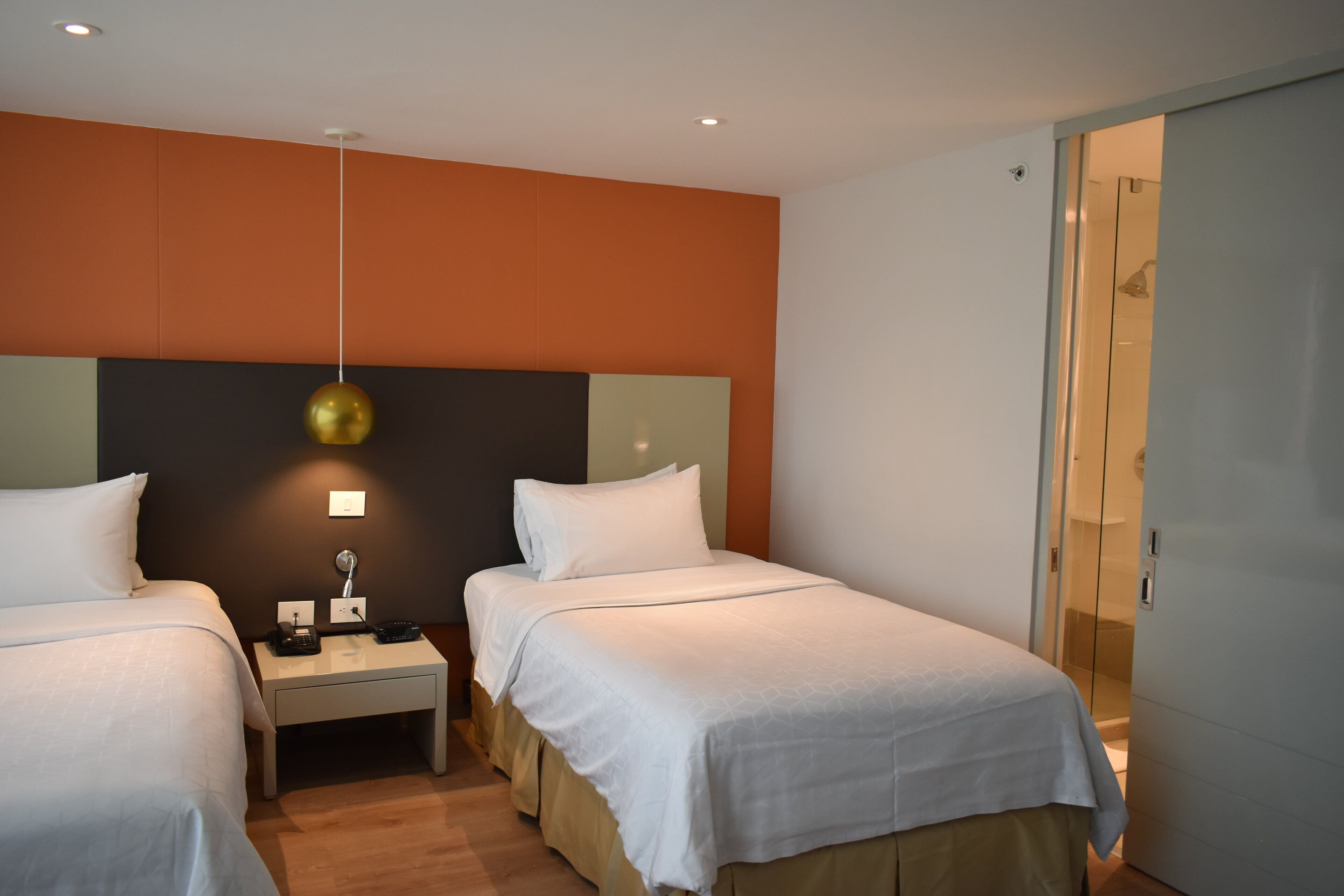 Et hotelværelse med to senge, et natbord med en lampe og et klædeskab.