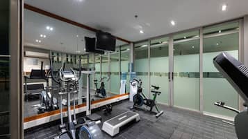 A modern gym with various exercise equipment, a large mirror, and a television.
