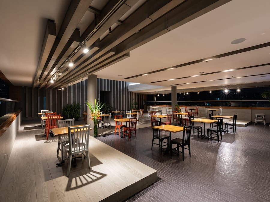 Un restaurante espacioso con múltiples mesas y sillas, un diseño de techo moderno y una zona de bar.