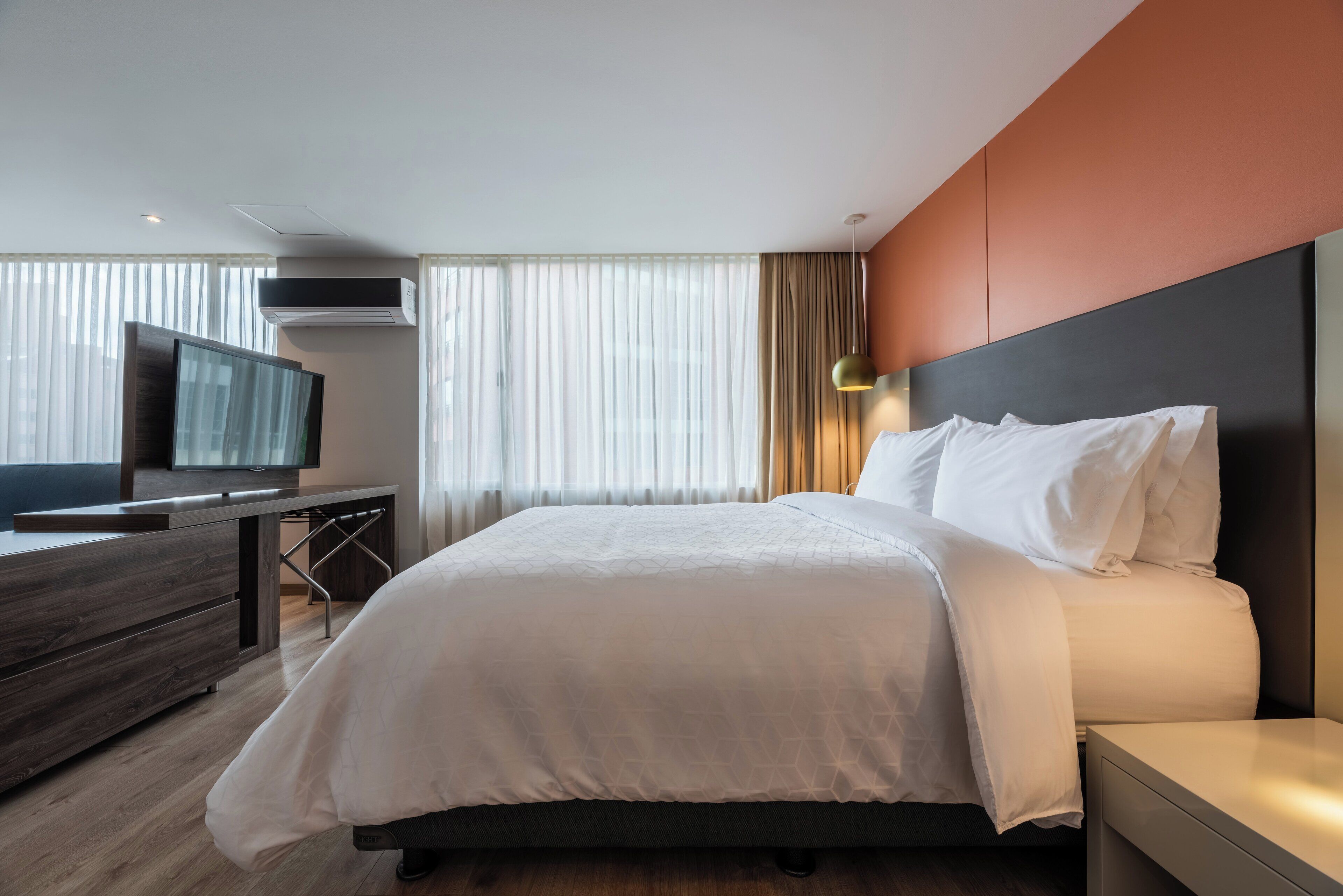 A modern hotel room with a large bed, a TV on a wooden desk, and a window with curtains.