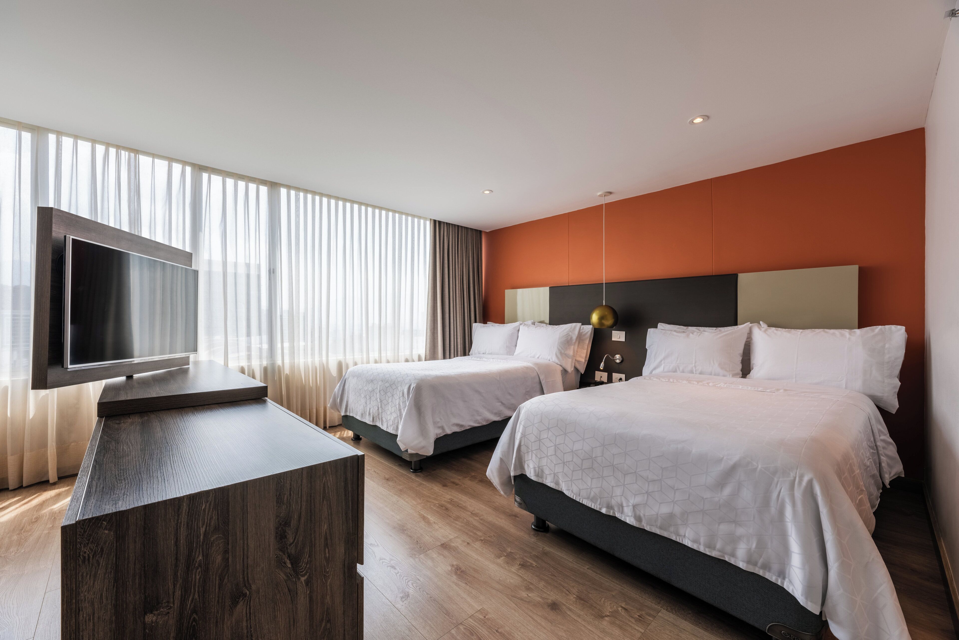 A hotel room with two beds, a TV, and a wooden desk.