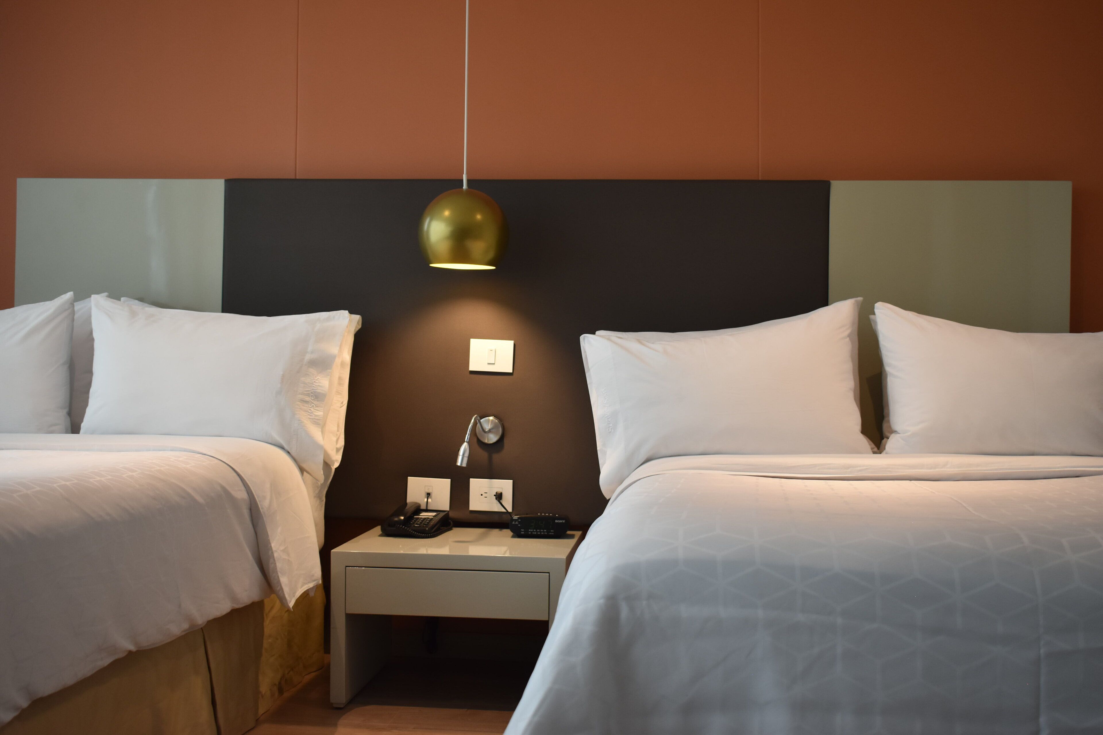 Une chambre d’hôtel avec deux lits, une table de chevet avec une lampe et un luminaire fixé au mur.