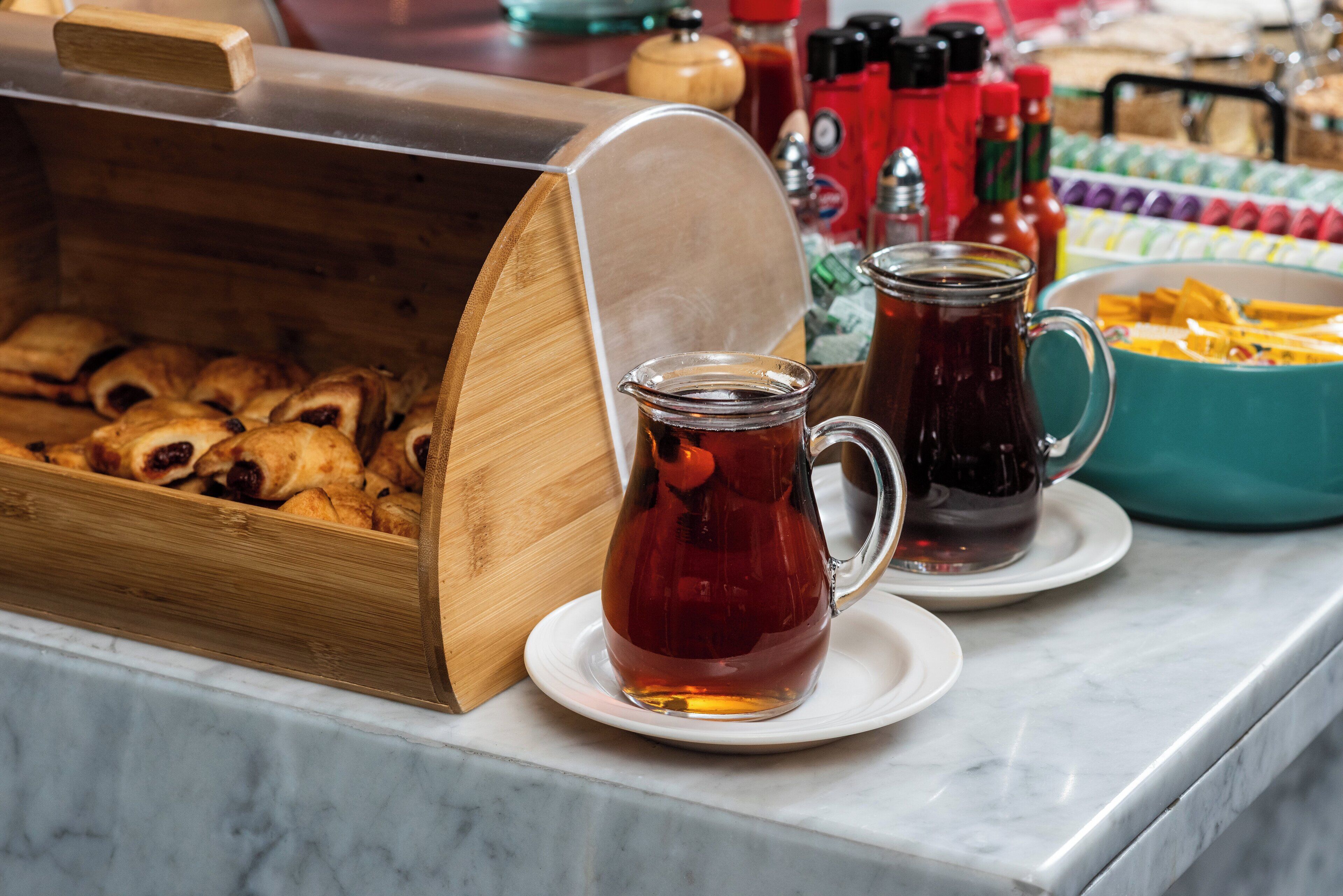 Un bufé con un expositor de madera que contiene pasteles, dos tazas de té y condimentos en la barra.