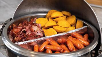 Un bufé con diversos alimentos, entre ellos salchichas, jamón y calabacín amarillo.
