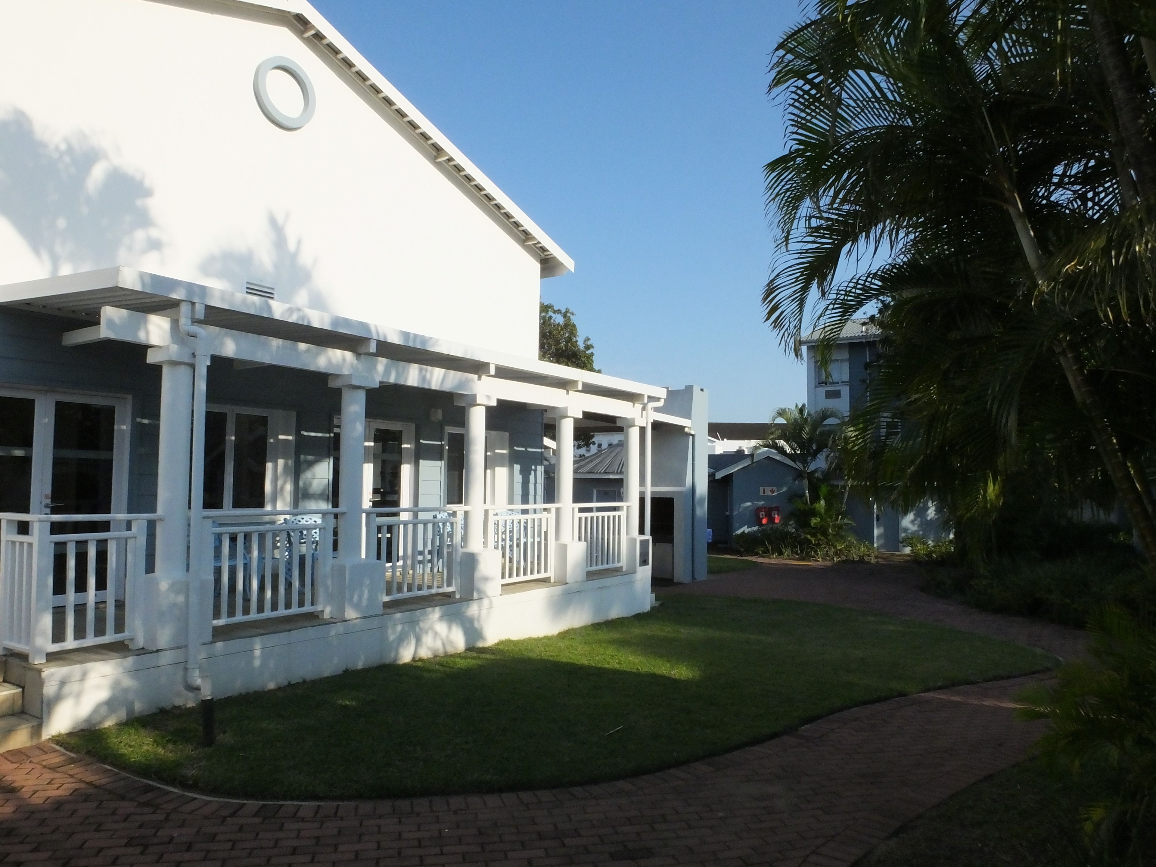 A white building with a covered porch and a brick pathway leading to it.