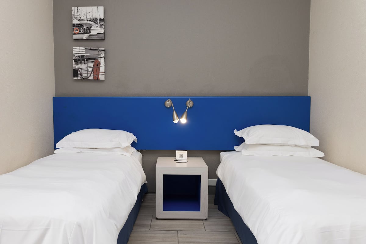 A hotel room with two beds, a blue headboard, and a small bedside table with a lamp.