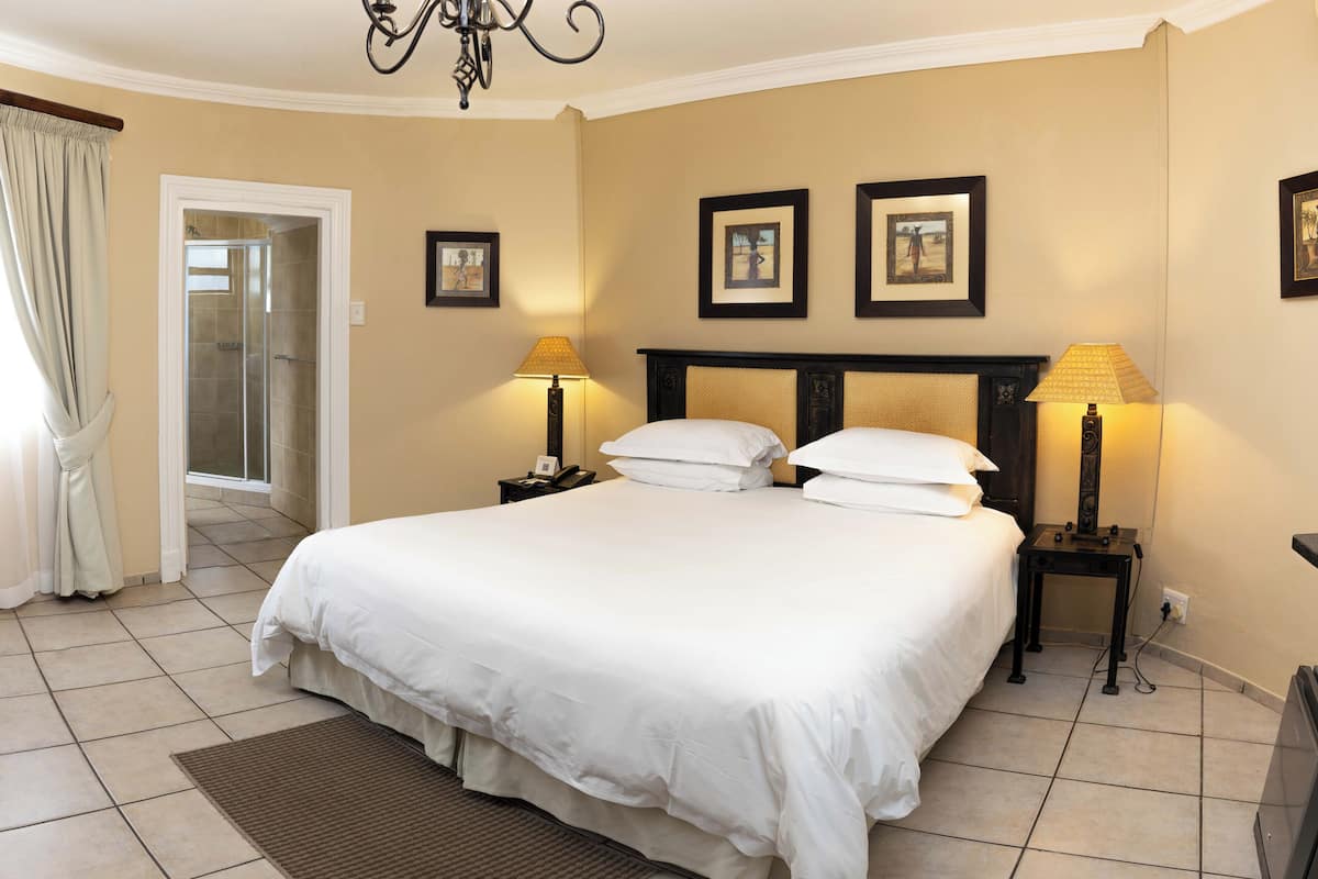 A hotel room with a large bed, two bedside tables with lamps, a door leading to a bathroom, and three framed pictures on the wall.