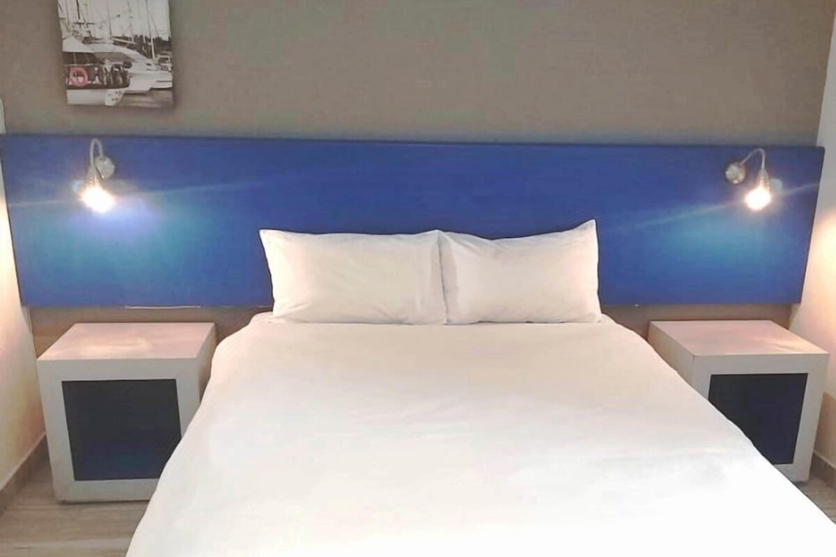 A hotel room with a bed, two bedside tables, and a headboard with wall-mounted lights.