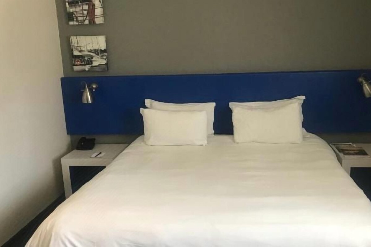 A hotel room with a large bed, two bedside tables, and a blue headboard.