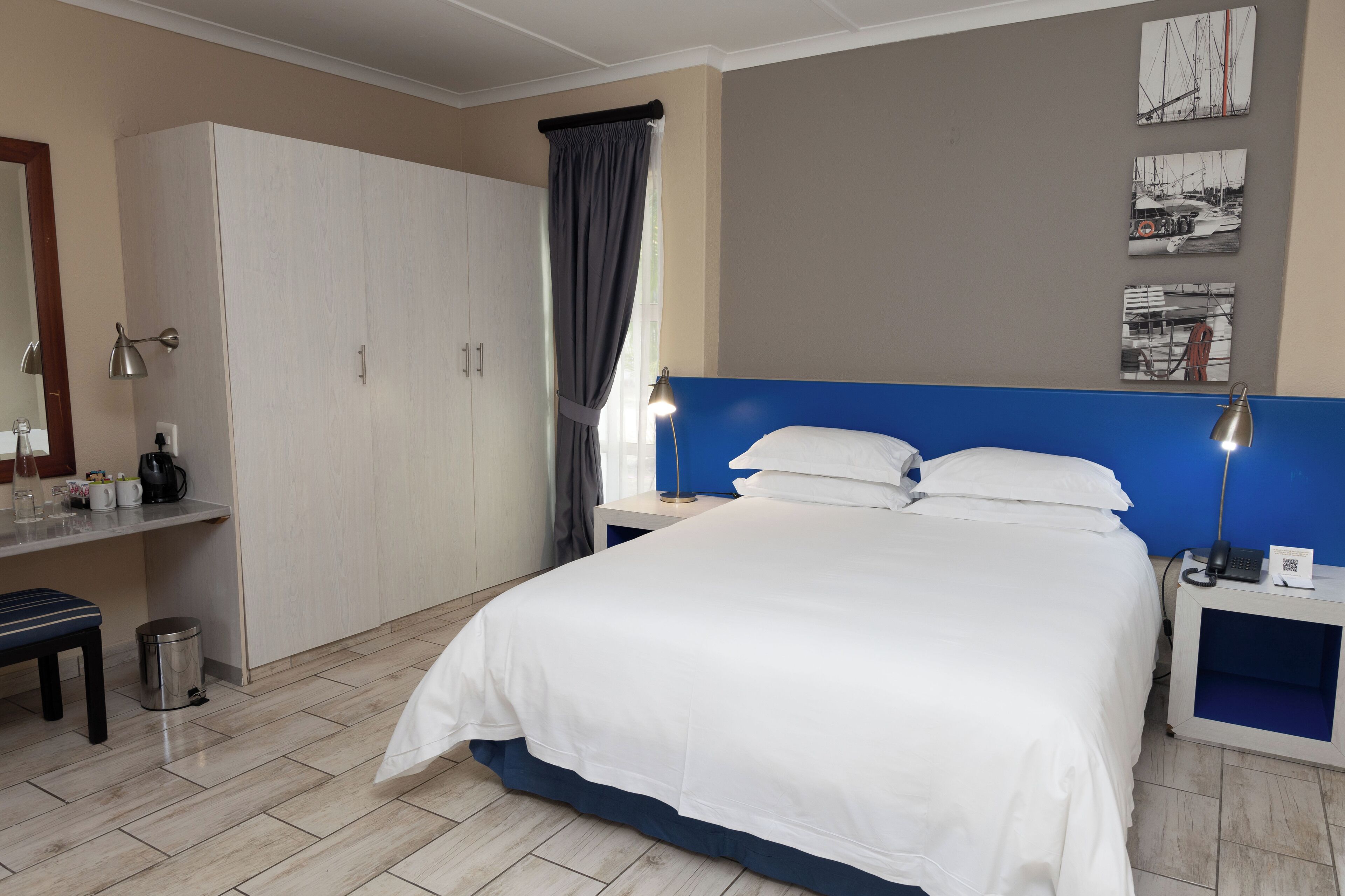 Quarto de hotel com uma cama, uma escrivaninha com luminária, um guarda-roupa e uma lixeira.